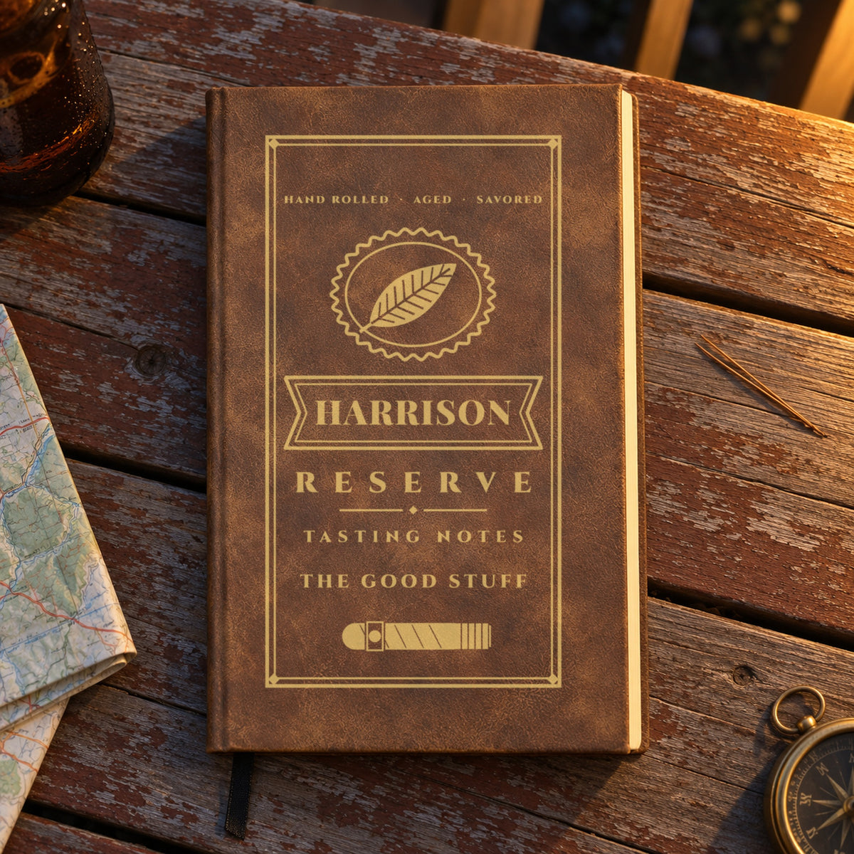 Brown engraved cigar journal for him with Harrison on the band and The Good Stuff, on a weathered porch table at golden hour